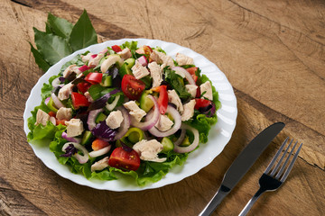 Summer fresh salad made of tomato, ruccola, chicken breast, arugula, crackers and spices and other different vegetables on wooden background