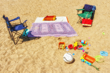 Relax with children on beach on golden yellow sand. Children toys are scattered in sand.