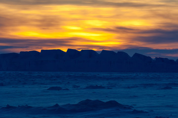 Obraz premium The frozen Weddell Sea in Antarctica at sunset with icebergs in the disdance.
