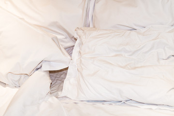 Close-up of rumpled bed with white crinkled pillows in hotel sleeping room, monochrome image