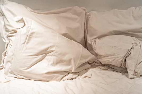 Close-up of rumpled bed with white crinkled pillows in hotel sleeping room, monochrome image