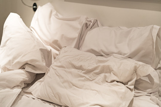 Close-up of rumpled bed with white crinkled pillows in hotel sleeping room, monochrome image