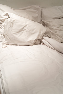 Close-up of rumpled bed with white crinkled pillows in hotel sleeping room, monochrome image
