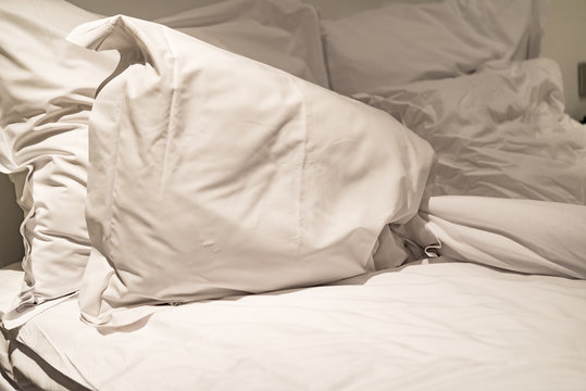 Close-up of rumpled bed with white crinkled pillows in hotel sleeping room, monochrome image