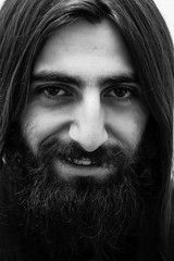 Closeup black-and-white portrait of a bearded man with long hair. Look at the camera.