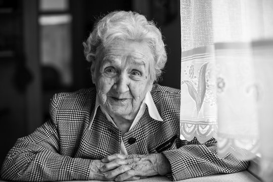 Elderly woman, black and white portrait, sitting at table in the house.