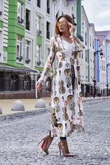 Woman walk on the street city style fashion casual elegant high heel catalog of clothes beautiful lady romantic date accessory sunglasses summer silk dress luxury lifestyle.