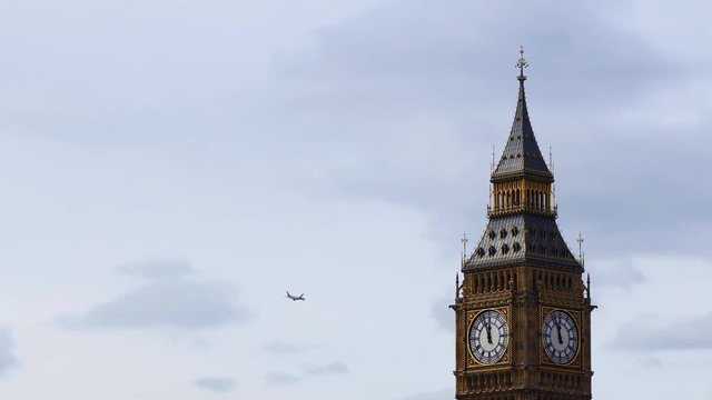 Aircraft flying in the sky behind the top of famous London landmark the Elizabeth or Big Ben clock tower at nearly twelve o'clock in the day, noon, midday.
