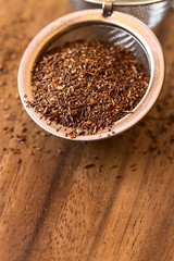 Rooibos herbal tea in strainer on wood, photographed with natural light (Selective Focus, Focus one fourth into the leaves in the strainer)