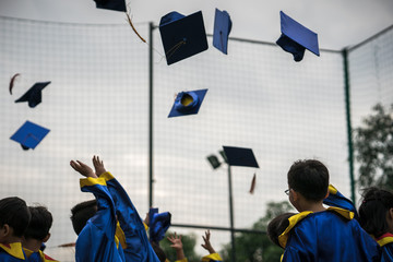 Preschool kids wearing graduated dress throwing cap and diplomat in sky in graduated celebration...