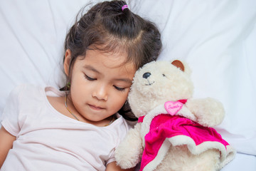 Cute asian little child girl with her teddy bear and lying in bed with sad moody at home