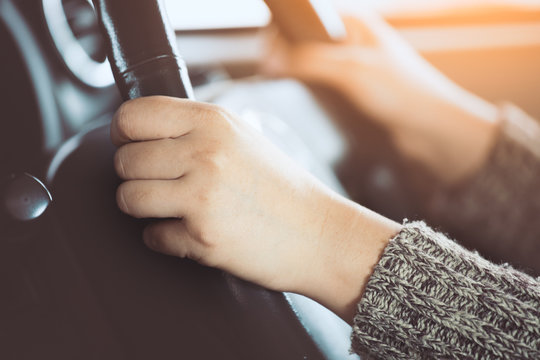 Woman hand holding on black steering wheel while driving a car in vintage color tone