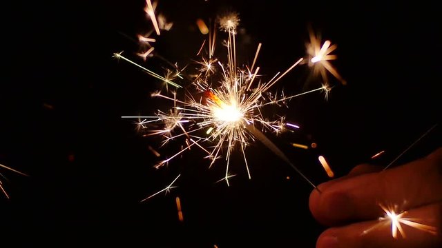 Slow Mo. Party burning sparkler closeup in male hand on black background. Bengal fire a type of stick with the thick paste of metallic fuel, produces tiny glowing sparks that shoot off in all directio