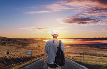 Young man with backpack walking on the country road in sunset