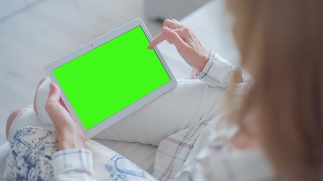 Young Woman in white jeans sitting on couch uses Tablet PC with pre-keyed green screen. Few types of gestures - scrolling up and down, tapping, zoom in and out. Perfect for screen compositing