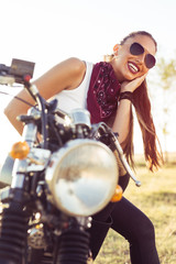 Outdoor lifestyle portrait of young biker woman sitting on a vintage custom motorcycle