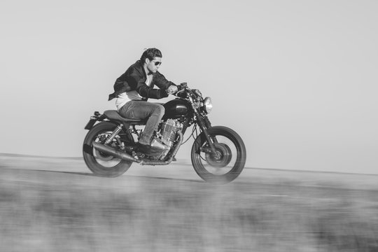 Young man riding a vintage motorcycle. Camera panning for motion blur.