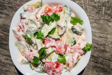 Fresh salad with tomato, cucumber, onion, parsley and mayonnaise on rustic wooden table