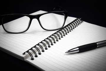 Notebook glasses and pen on black background.