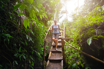 Woman tourist with backpack goes down bamboo stairs in jungle into the cave