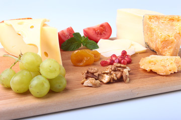 Assortment of cheese with fruits, grapes, nuts and cheese knife on a wooden serving tray.