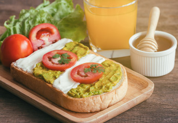 Open sandwich for breakfast or lunch. Healthy sandwich spread with cream cheese,  avocado and tomato.  Avocado and cream cheese open sandwich style serve with orange juice on rustic wood table.
