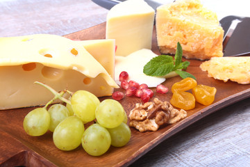 Assortment of cheese with fruits, grapes, nuts and cheese knife on a wooden serving tray.