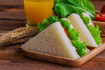 Piece of sandwich ham cheese with lettuce and tomato on wood plate. Homemade sandwich served with orange juice for breakfast or lunch. Delicious ham cheese sandwich ready to served on wood table.
