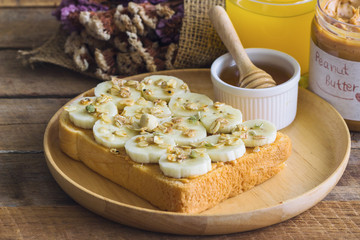 Banana peanut butter toast sandwich on wood plate with honey. Homemade open sandwich spread with peanut butter on top with banana slice and granola. Delicious healthy sandwich for breakfast or lunch.