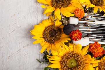 Fototapeta premium Make up brushes next to beautiful wild flowers on wooden background