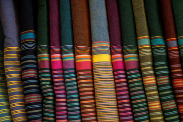 Row of colorful traditional strip pattern fabric textile rolls in local shop