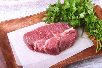 Raw beef steak with spices Leaves of coriander on wooden cutting board. Ready for cooking.