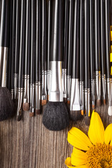 Make up brushes next to flowers on wooden background