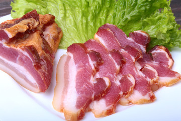 Fresh homemade smoked bacon with leaves lettuce on white plate. Selective focus.