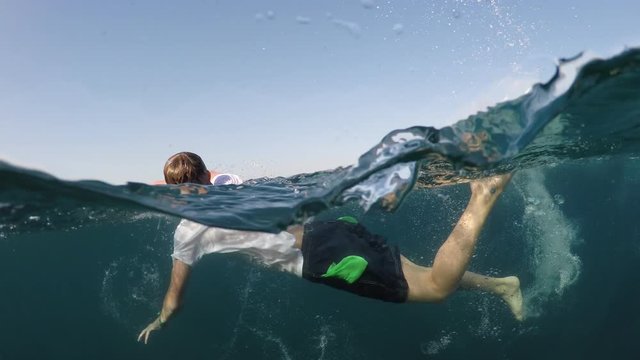 young man in a white shirt is swimming on the sea, half underwater close up, raw, 4k