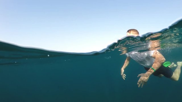 young man in a white shirt is swimming on the sea, half underwater close up, raw, 4k
