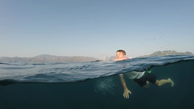 young man in a white shirt is swimming on the sea, half underwater close up, raw, 4k
