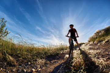 Naklejka premium Young cyclist riding mountain bicyclist against beautiful sunset in the countryside.