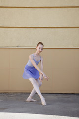 Fototapeta premium Ballet dancer dancing on street. Young ballerina on yellow background full length