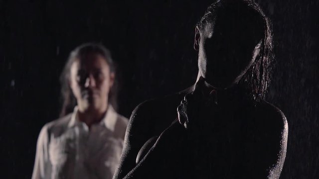 girls lesbian fight. they stand in the dark in the rain. one naked and touching your face with your hand you can see her silhouette. another woman stands in the background.