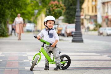 Fototapeta premium Little boy kid in helmet ride a bike in city park. Cheerful child outdoor.