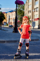 Girl riding on roller skates in skatepark summer outdoor. Child in a red suit for the rollers