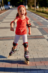 Girl riding on roller skates in skatepark summer outdoor. Child in a red suit for the rollers