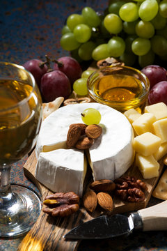 snacks, wine and Camembert cheese on a dark background, vertical, closeup