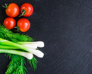 Green onions, tomatoes, dill and pita bread lying on a black background.