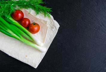 Green onions, tomatoes, dill and pita bread lying on a black background.
