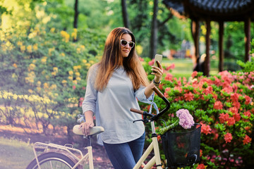 A woman with city bicycle in a summer outdoor park.