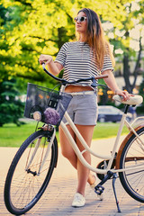 A woman with city bicycle in a summer outdoor park.