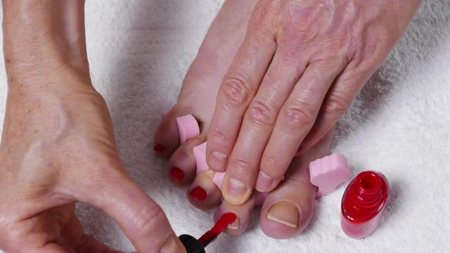 Closeup woman painting nails of her feet, applying red toenails. Foot pedicure, body care. Timelapse 4K ProRes HQ codec
