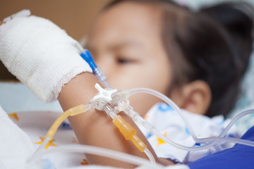 Child's patient hand with saline intravenous (iv) drip holding smartphone,tablet in the hospital